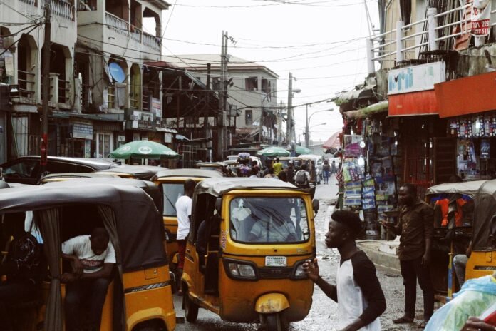 A busy Lagos street lined with shops, tricycles and pedestrians