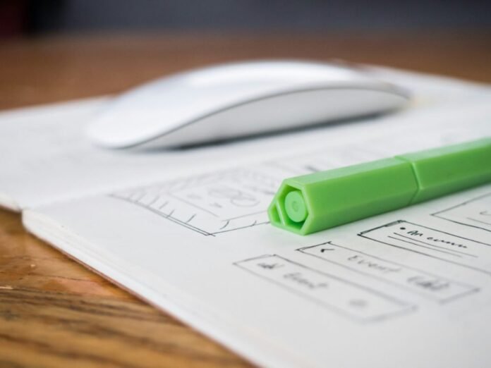 Hand-drawn UX wireframe sketches on paper beside a computer mouse