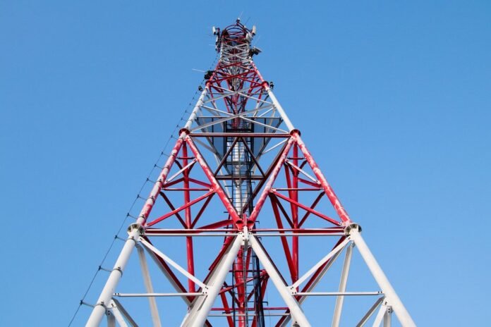 Red and white mobile network tower against a blue sky